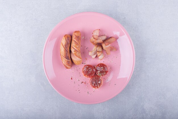 Various shaped fried sausages on pink plate.