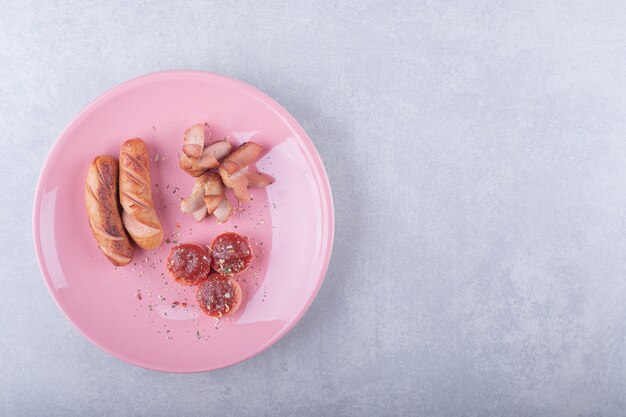 Жареные сосиски различной формы на розовой тарелке.