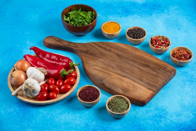 Various spices around wooden board with plate of vegetables.