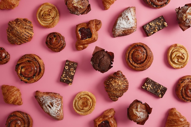 Various sweet appetizing bakery products isolated over rosy background. Various croissants, buns powdered with sugar, cookies filled with jam, chocolate muffin, yummy rolls. Confectionery assortment
