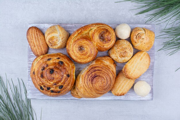 Various sweet pastries and rolls with cookies on wooden board.