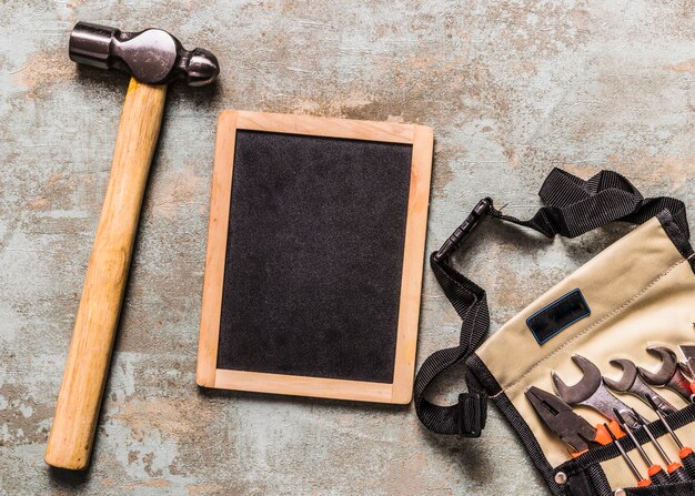 Various tools in toolbag near slate and hammer on rust wooden desk