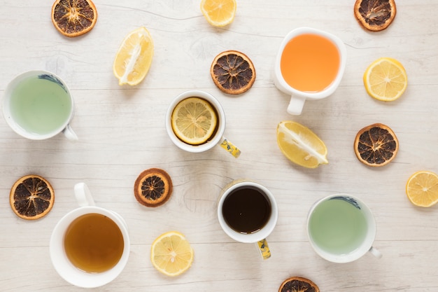 Foto gratuita vari tipi di tè in tazza di ceramica; fette di pompelmo secco con limone su fondo di legno