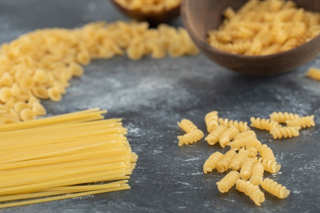 Various types of uncooked pasta with wooden spoons.