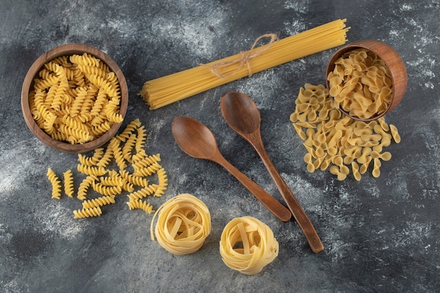 Various types of uncooked pasta with wooden spoons. 