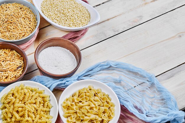 Various uncooked pasta bowls on wooden table with blue tablecloth.