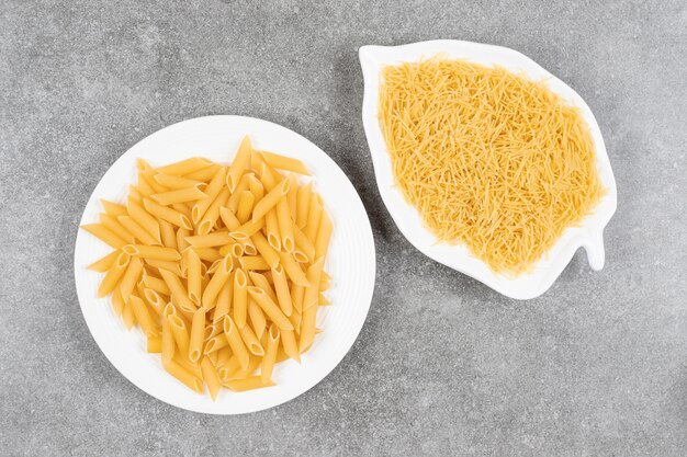 Various uncooked pasta on white plates