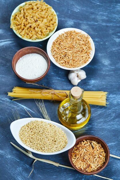 Various uncooked pasta with a bottle of oil and garlic.