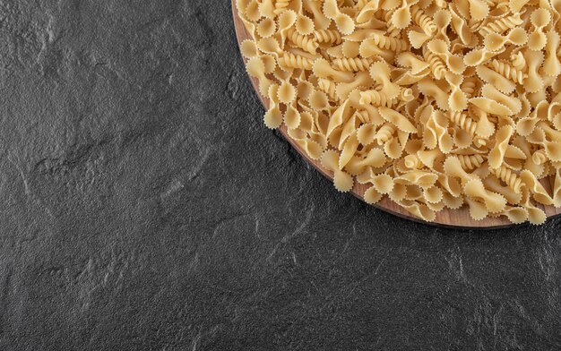 Various uncooked pasta on wooden plate.