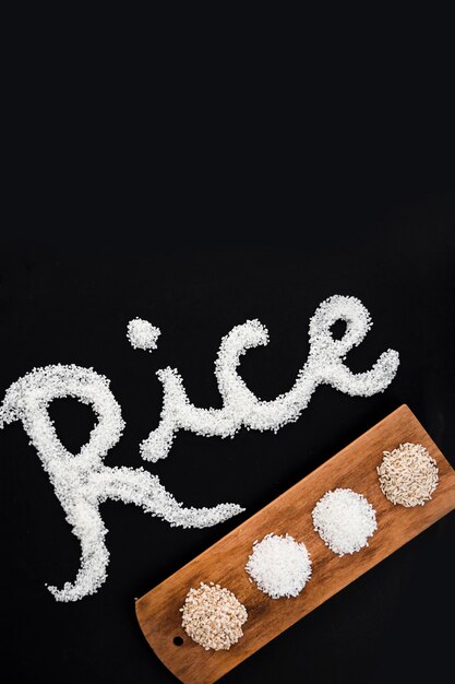 Various uncooked rice on wooden tray with text on black backdrop