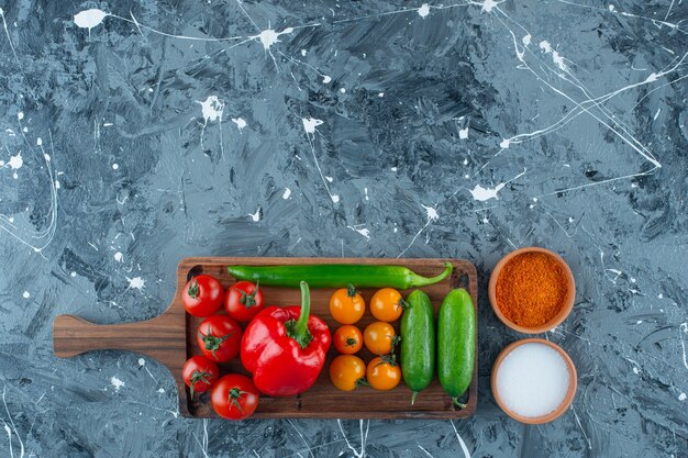 Various vegetables on a board next to salt and spice, on the marble background. 