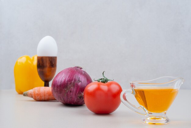 Various vegetables with egg and oil on white surface