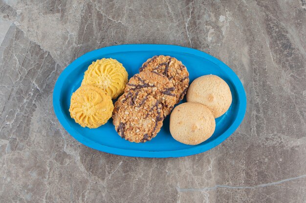 Variously cookies on a wooden plate on marble.