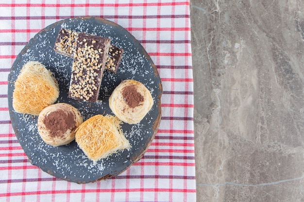 Variously desserts on a board on tea towel on marble.