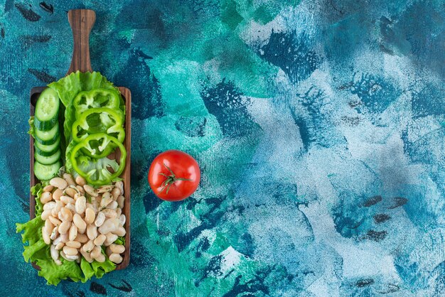 Variously vegetables and beans on board on blue.