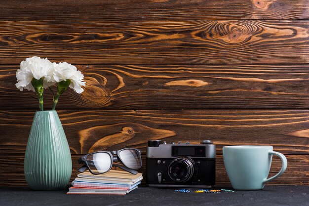 花瓶;本めがねペーパークリップ;木製の背景に対して黒い机の上のカップとレトロなカメラ