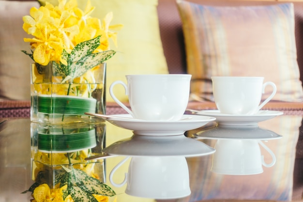 Foto gratuita vaso di fiori e tazza di caffè bianco sul tavolo e cuscino sul divano