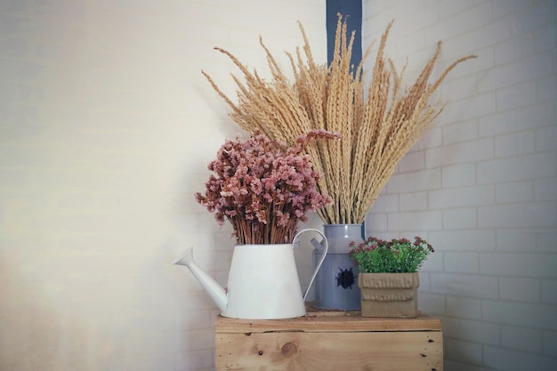 Ваза с букетом розовых цветов и сухими колосьями пшеницы на деревянном столе с фоном цементной стены