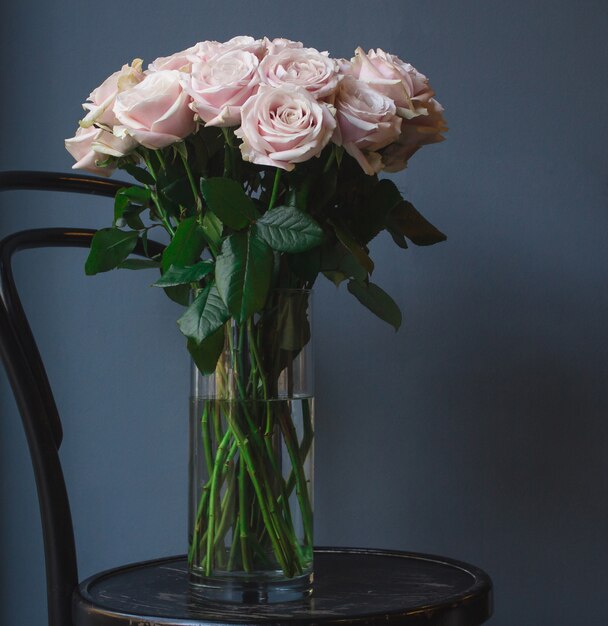 A vase of white pastel tone roses standing on an old rustic round ottoman chair