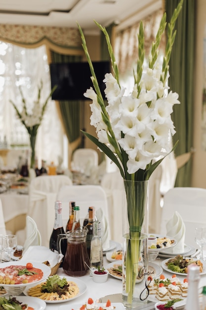 Vase with iris flowers stands on the table with food in a restaurant