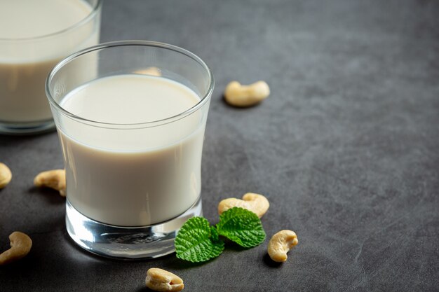 Vegan cashew milk in glass with cashews nuts on dark background