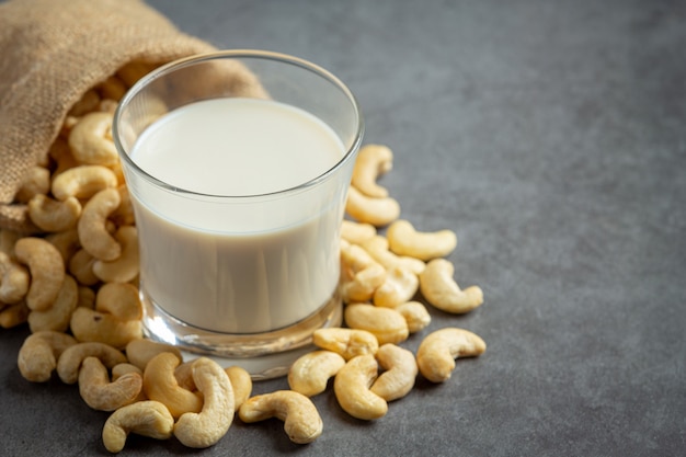 Веганское молоко из кешью в стакане с орехами кешью на темном фоне