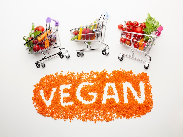 Vegan lettering with delicious vegetables in small shopping carts