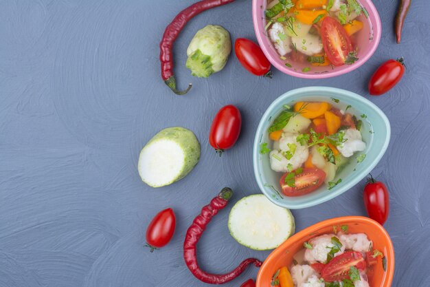 Vegetable broth soup in colorful cups on blue.