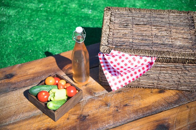 Vegetable crate; olive oil bottle and picnic basket on wooden table