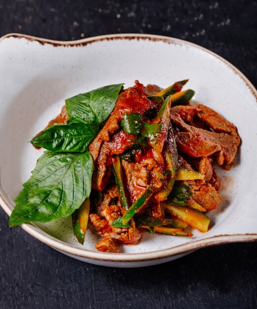 Vegetable meat stew with basilic leaves in a white bowl.