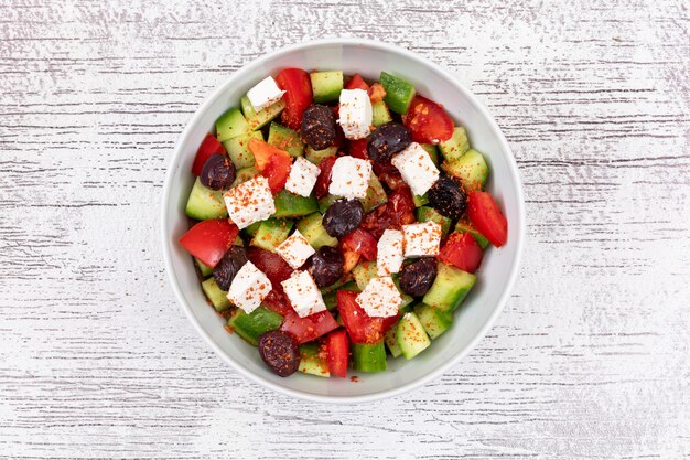Vegetable salad cheese cucumber tomato olive in a white bowl on the wooden surface top view healthy food
