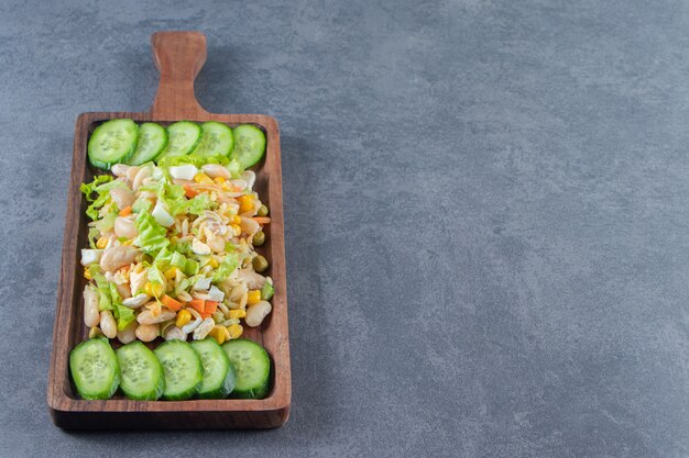 Vegetable salad and sliced cucumbers on a board, on the marble background.