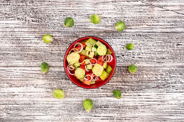 Vegetable salad surrounded by cabbage on white wooden surface