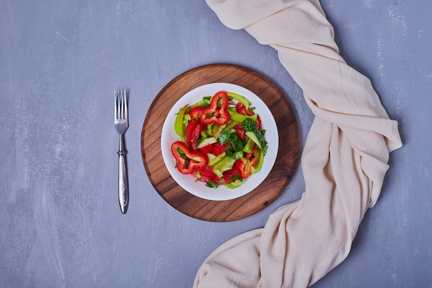 Foto gratuita insalata di verdure in un piatto bianco sull'azzurro