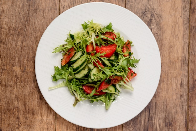 Vegetable salad in white round plate on wooden table. Macro from above.