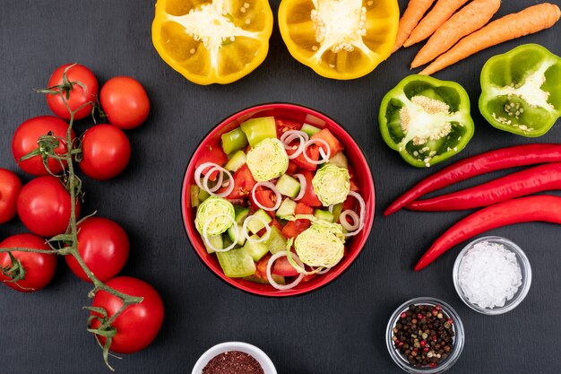 Vegetable salad with carrot tomatoes red onions yellow sweet pepper on a black surface