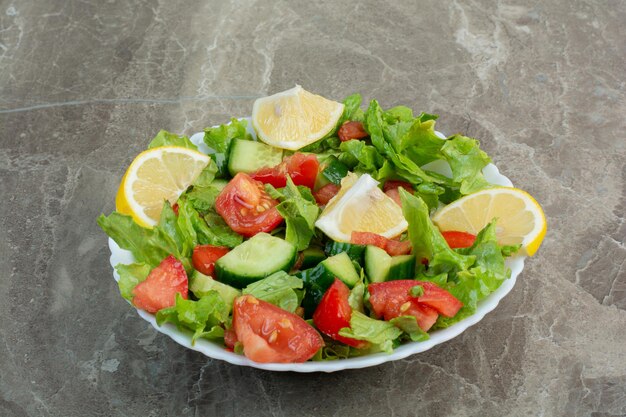 Овощной салат с ломтиками лимона на белой тарелке. Фото высокого качества