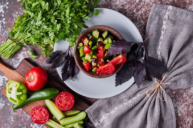 Vegetable salad in a wooden cup served with herbs, top view