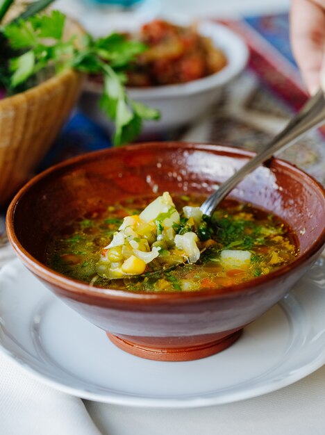 Овощной суп с бульоном и зеленью внутри коричневой миски.