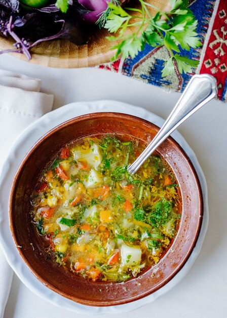 Vegetable soup with herbs inside brown bowl.