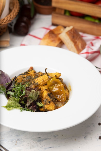 Vegetable stew with meat, corn pieces, chili pepper and vegetables, basilic, parsley in white plate. 