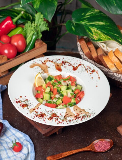 Vegetable, tomatoes, cucumber salad. salad with sumakh and lemon on the kitchen table inside white plate 