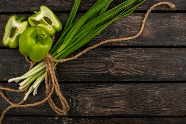 Vegetables cut green bell peppers along with tied green herbs on a brown rustic wooden desk