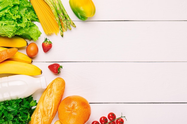흰색 나무 바탕에 야채, 과일 구색, 우유 한 병. 채식 건강 식품 개념입니다. 음식과 식료품 쇼핑.