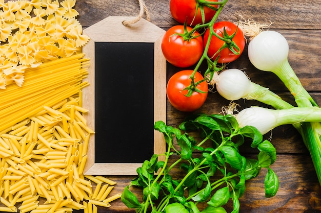 Vegetables and herbs near blackboard and pasta