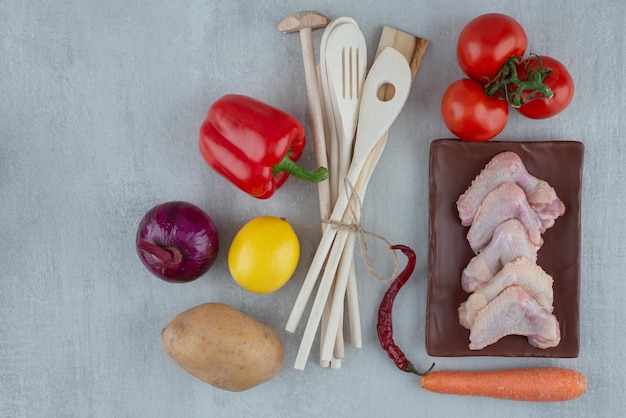 Vegetables, kitchen tools and raw chicken wings on gray surface.