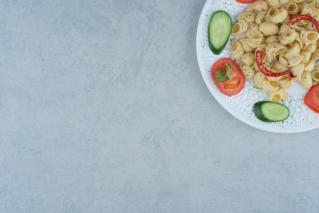 大理石の背景においしいマカロニと白いプレートの野菜サラダ