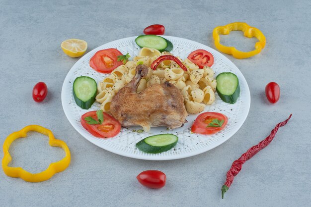 Салат из овощей на белой тарелке с пастой и курицей на мраморном фоне