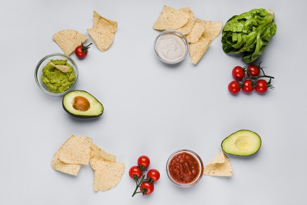 Vegetables and sauces in bowls among heaps of nachos