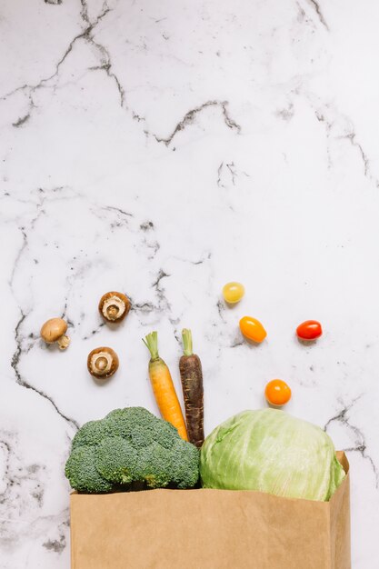 Vegetables spilling from brown paper bag on marble kitchen counter